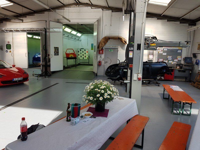 Eine überdachte Garage mit Sportwagen, Werkbänken und einem Tisch mit Blumen und Getränken.