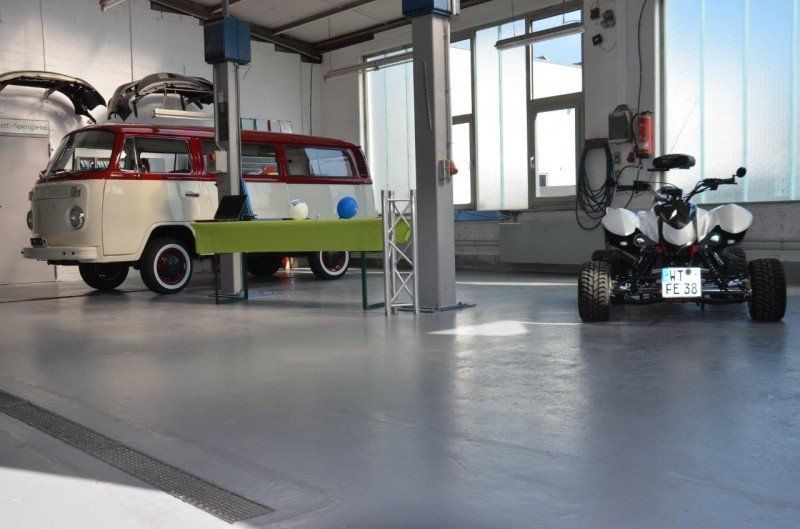 Ein Oldtimer-Lieferwagen und ein weißes Roboterauto in einer Garage mit Hebebühne und poliertem Boden.