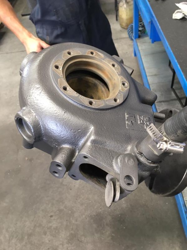 Primo piano di un alloggiamento di turbocompressore in metallo pressofuso grigio, tenuto in un'officina.