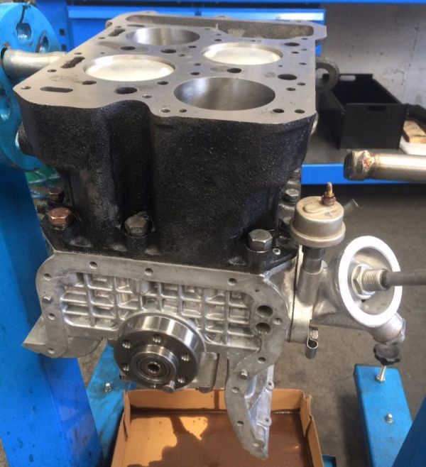 In un'officina, un blocco motore a quattro cilindri parzialmente smontato è montato su un supporto blu.