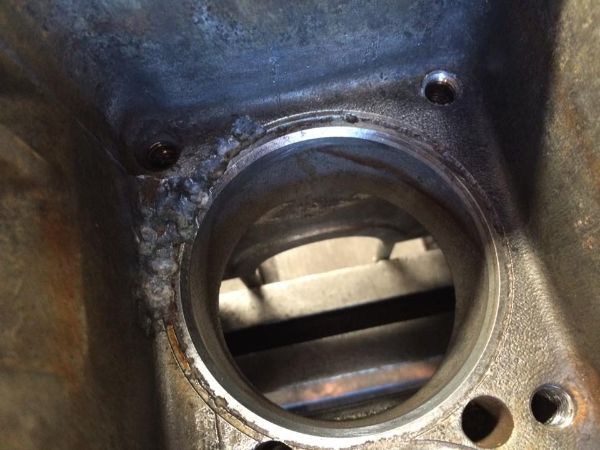 Primo piano dell'alesaggio di un cilindro di un motore in metallo lavorato, che mostra segni di saldatura ruvidi e irregolari sulla superficie circostante.