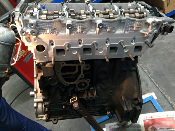 Un motore di un'auto smontato che mostra la testata in alluminio argentato montata sopra il blocco motore nero.