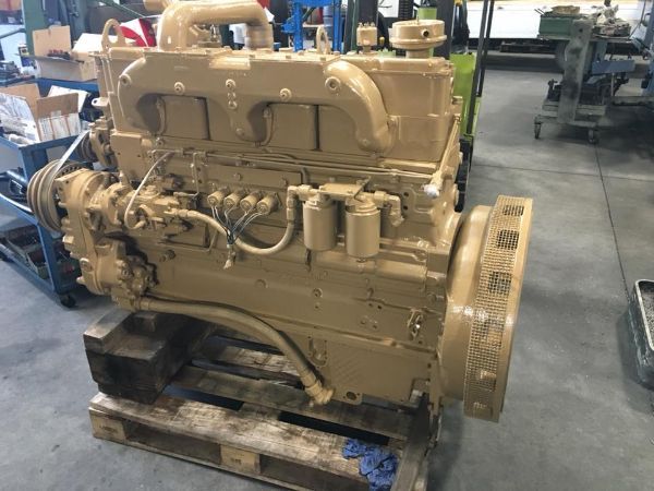Un motore diesel beige a sei cilindri montato su un pallet di legno in un'officina industriale.