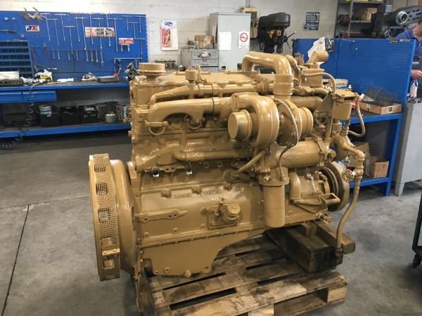 Un motore diesel industriale Caterpillar color beige è appoggiato su un pallet di legno all'interno di un'officina con pareti portautensili blu.