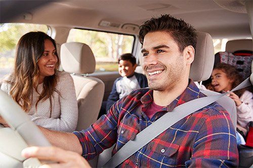 A man is driving a car with his family in the back seat.