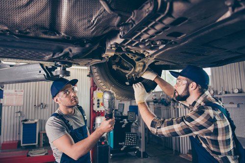 Two mechanics are working under a car in a garage.