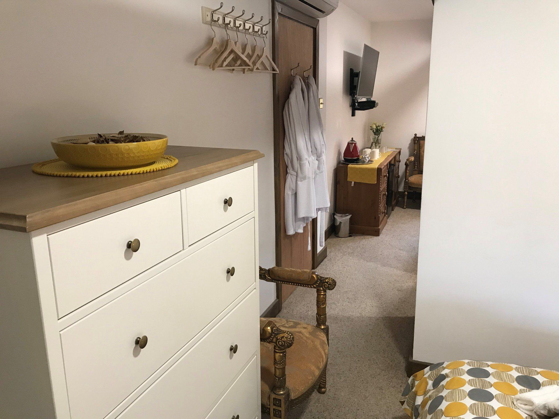 View across the front of a hotel room including a white dresser, door and 2 dressing gowns