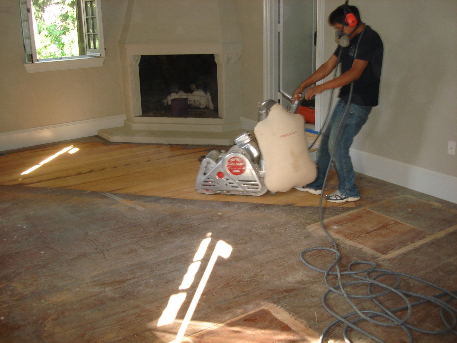 A man wearing headphones is sanding a floor