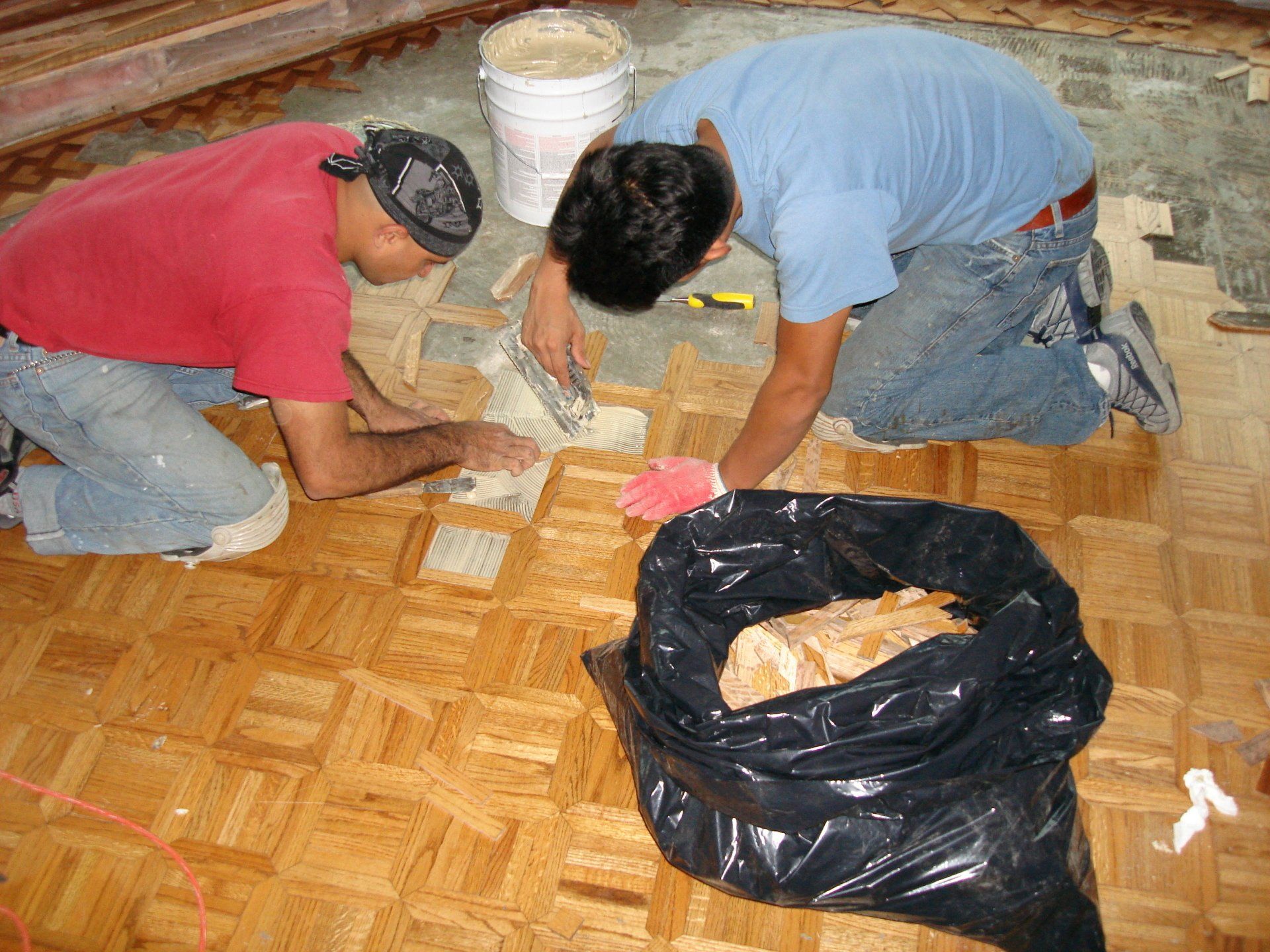 Two men are working on a wooden floor next to a black bag