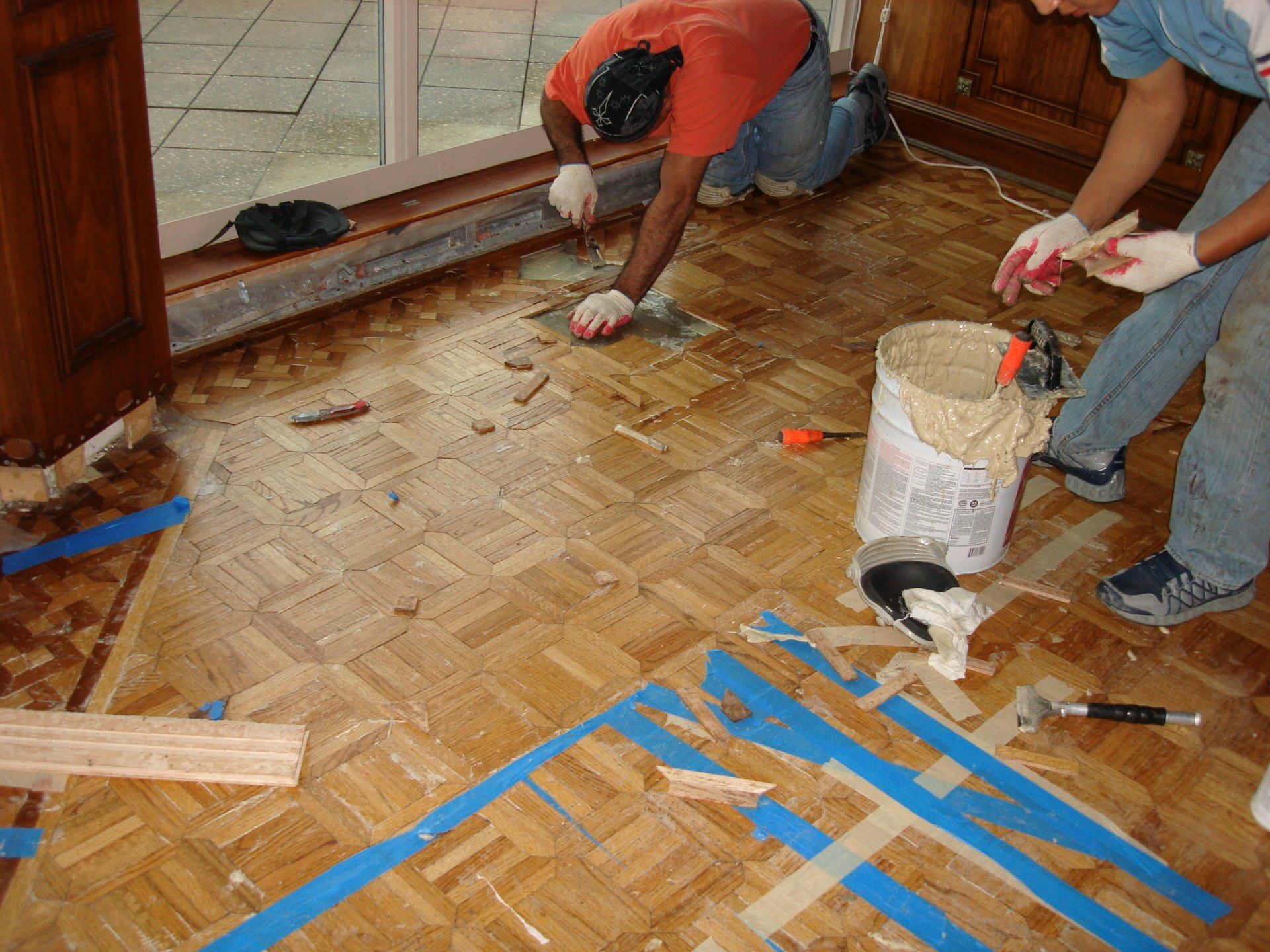 Two men are working on a wooden floor with blue tape