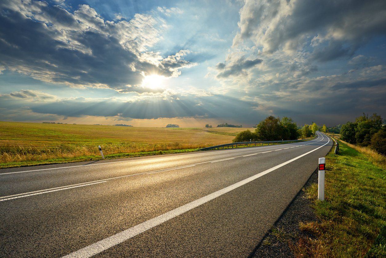 empty asphalt road in the middle of a big field with a cloudy sky and afternoon sun