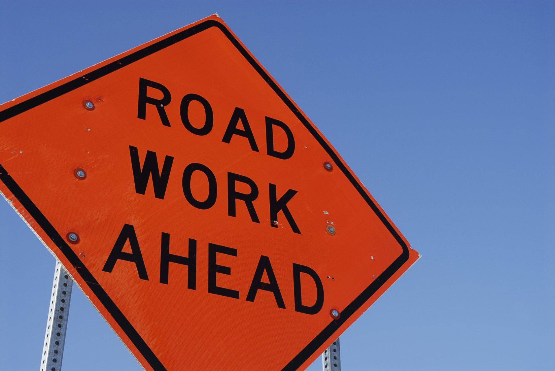 orange sign that reads road work ahead against a blue sky