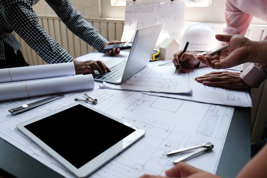 A work meeting with the table covered in architectural drawings, a tablet and a laptop