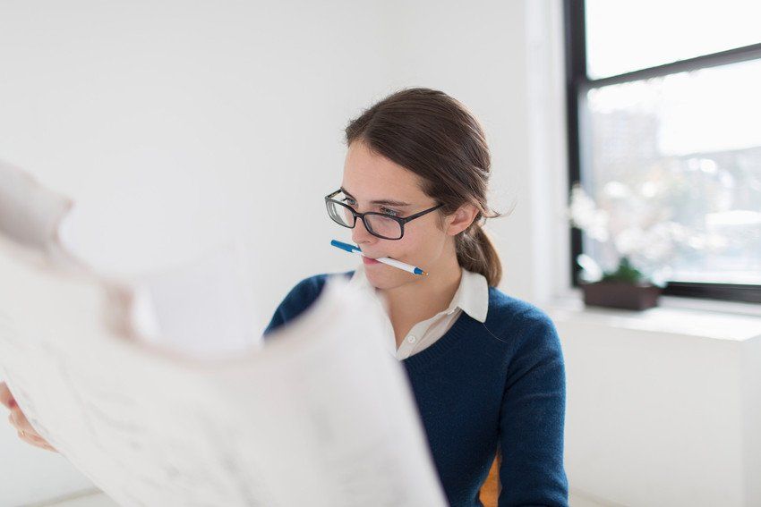 Young woman wearing glasses with a pen in her mouth looking over papers