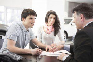 Couple signing paperwork with a car salesperson in a car dealership.