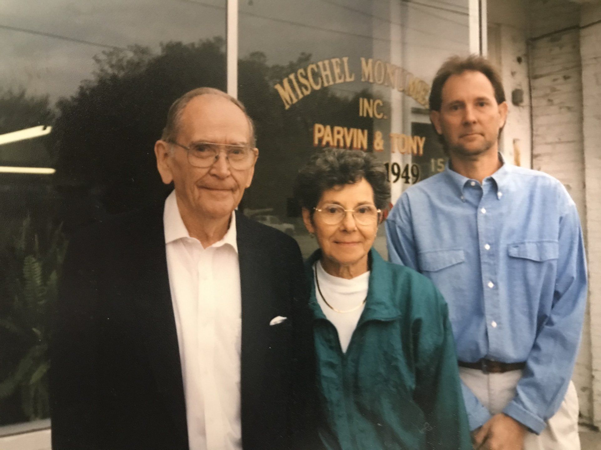 A man and two women standing in front of a window that says mischel