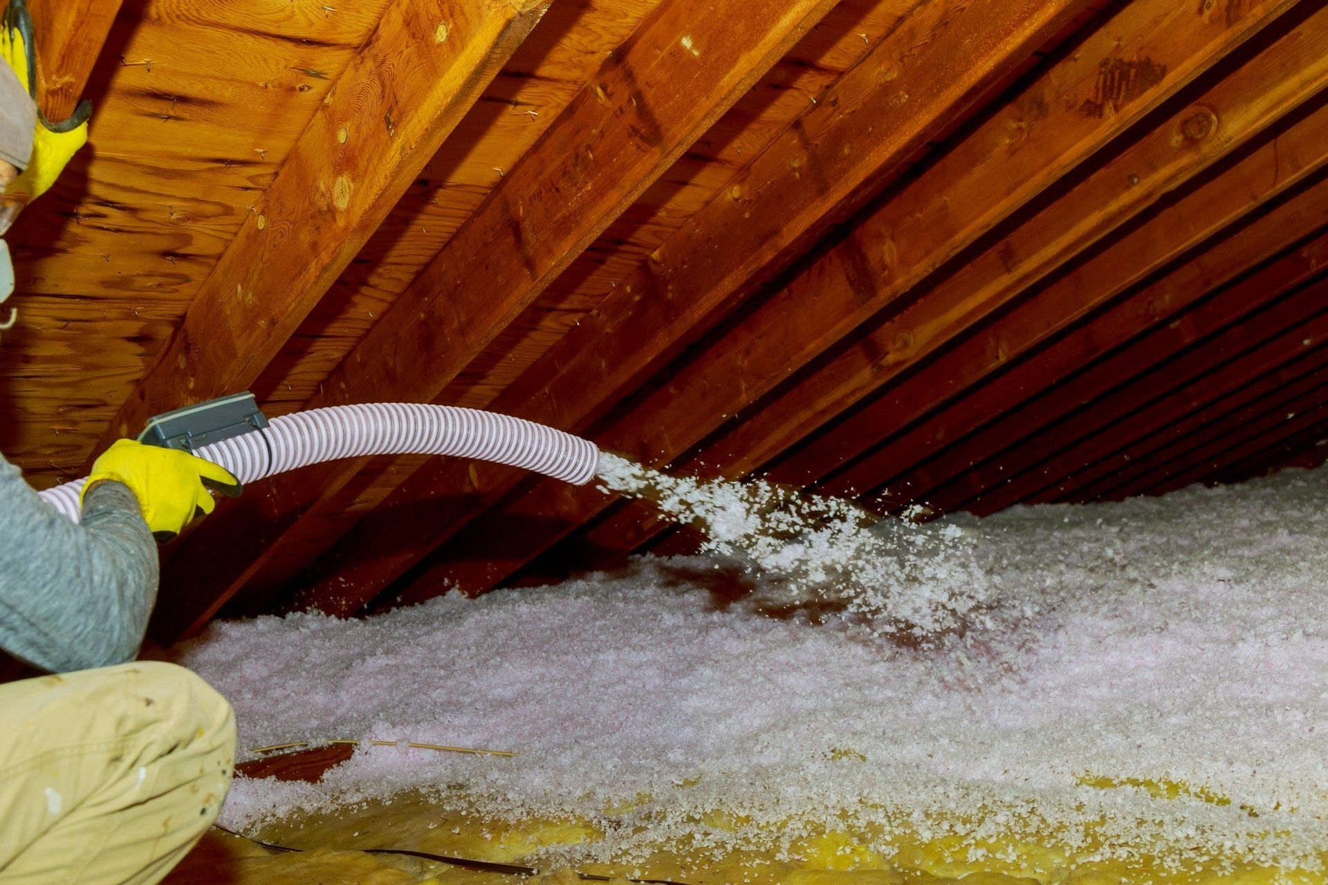 Worker blowing insulation into an attic with a hose under a slanted wooden roof
