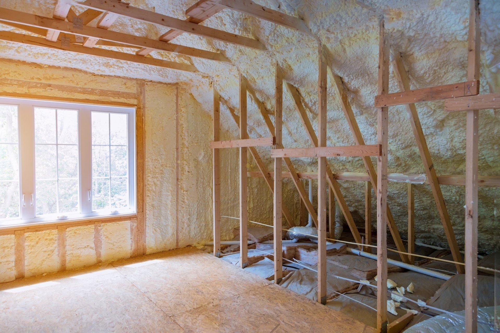 Interior under renovation with exposed wooden framing, insulated walls, and a window letting in daylight