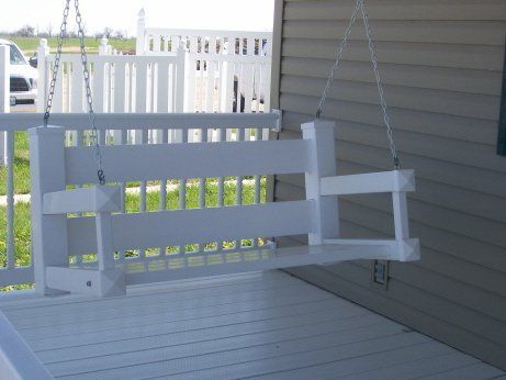 White wooden porch swing hanging from chains on a white porch.