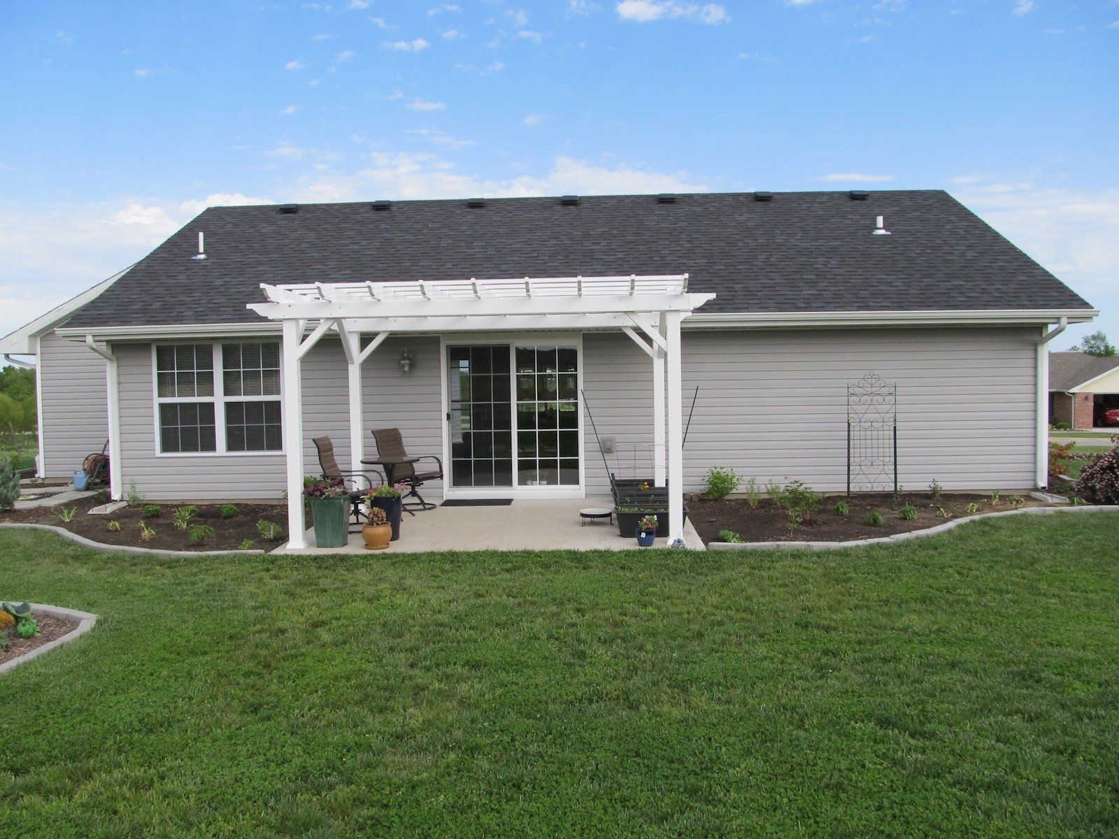 Backyard with gray siding, pergola over patio door, lawn, and blue sky.