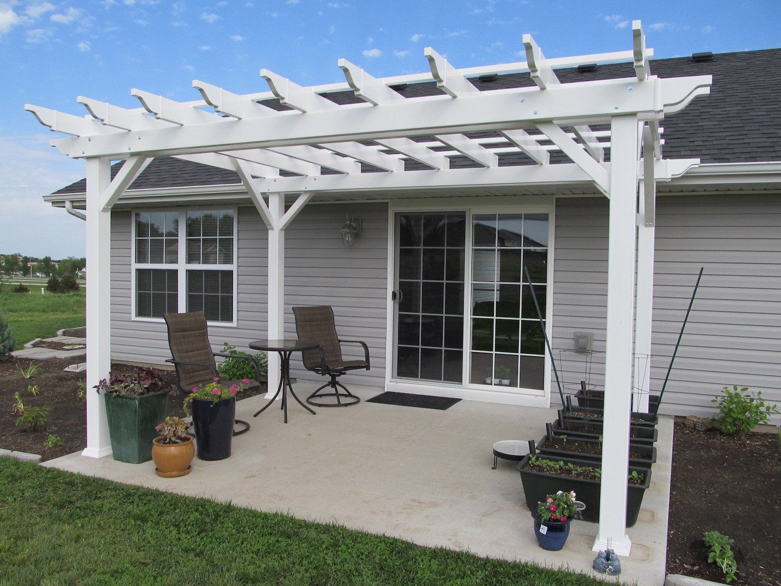 White pergola over a patio with sliding glass door and two chairs.