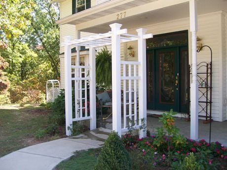 White trellis archway over a front porch entrance, with blooming flowers.