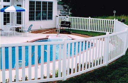 White picket fence surrounds a backyard swimming pool and a house.