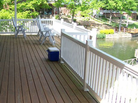Wooden deck with white railing and chairs overlooking a body of water. A blue cooler is on the deck.