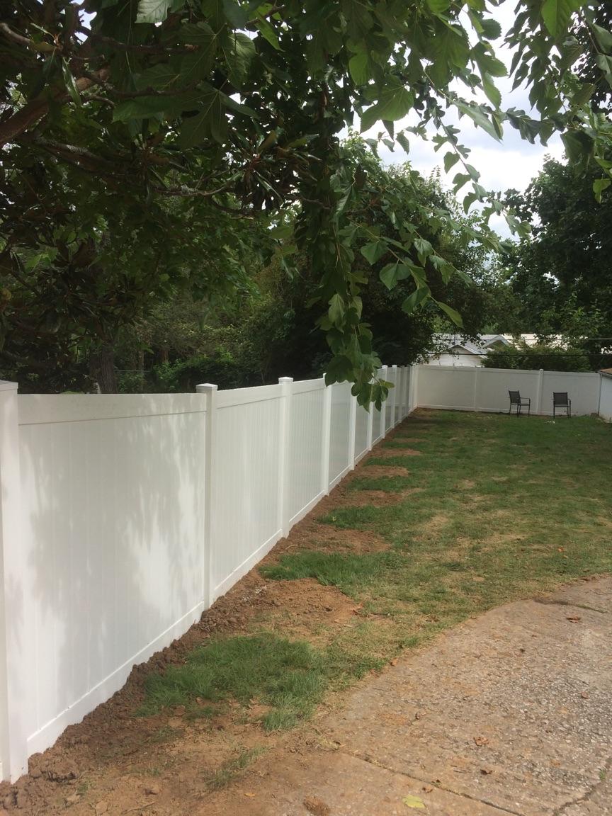 White vinyl fence bordering a yard with grass and trees on a cloudy day.