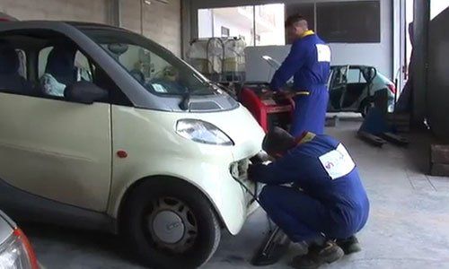 Un meccanico con una tuta blu chinato a terra mentre ripara la parte anteriore di una macchina bianca