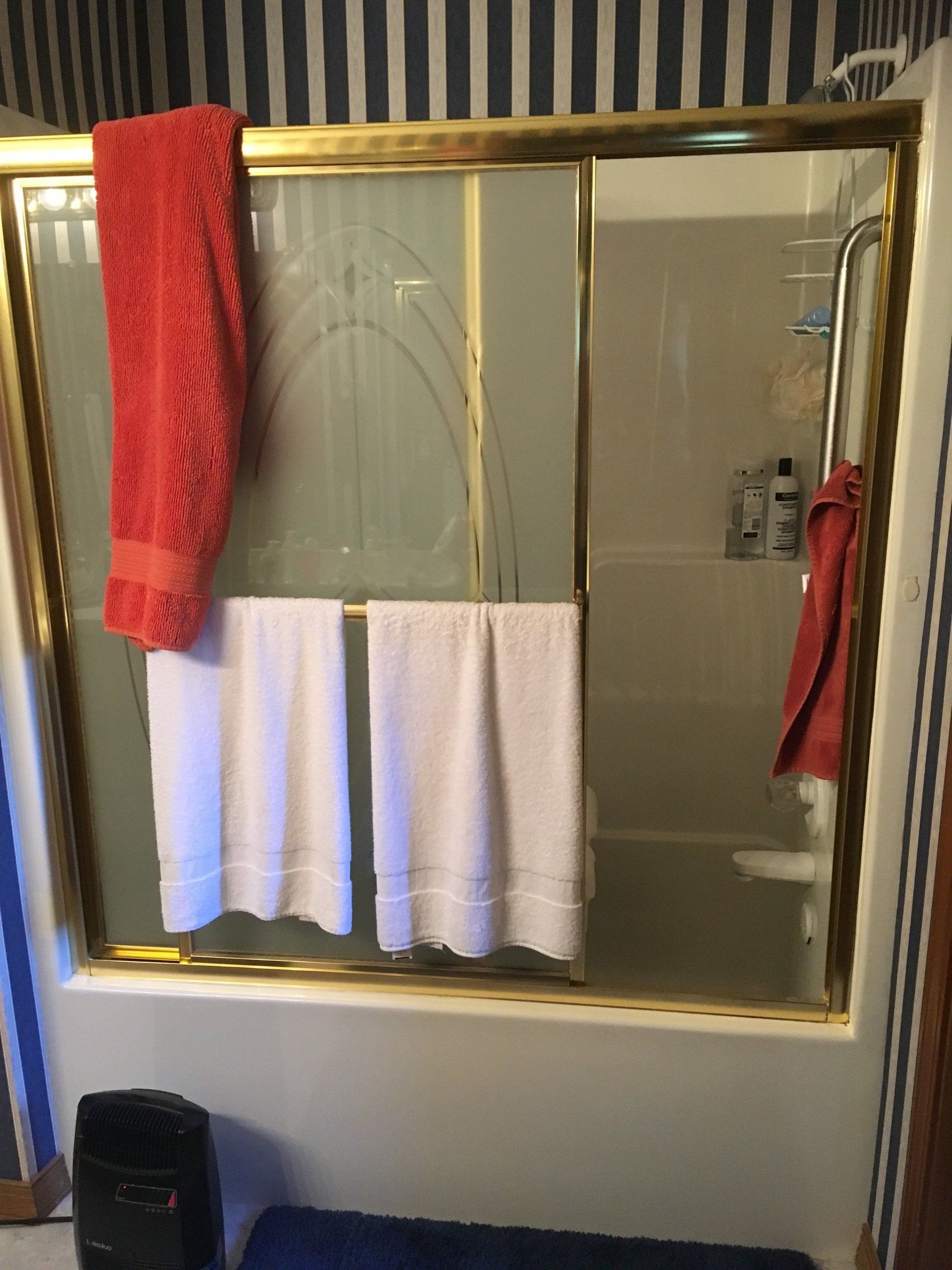 A bathroom with two towels hanging from a shower door.