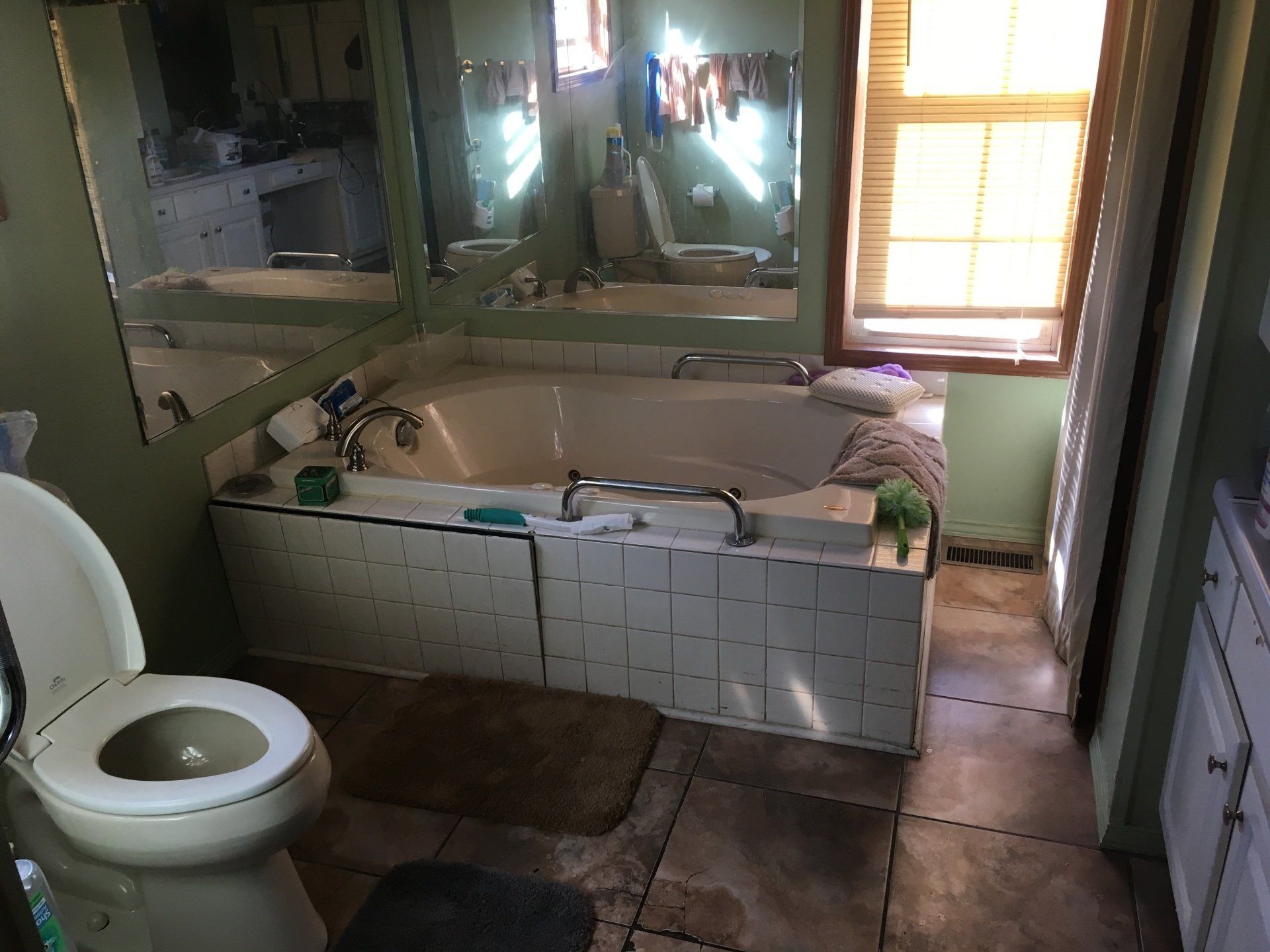 A bathroom with a toilet , tub , mirror and window.