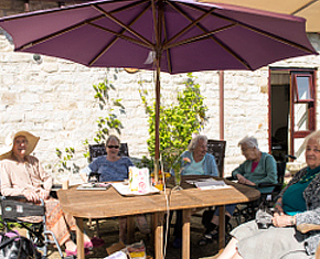 elderly people sitting under a big umbrella