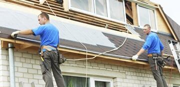 Roofing Work with Flex Roof Two workers in blue shirts installing wiring on a building exterior under a window ledge