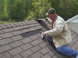 Roofer at Work Worker kneeling on a shingled roof, using a tool near a vent pipe