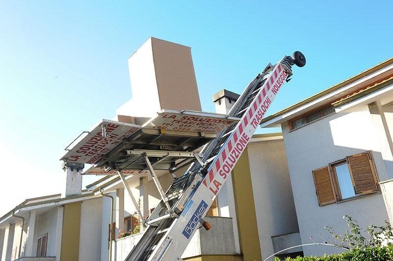 Ascensore mobile che solleva una grande scatola ai piani superiori di un edificio sotto un cielo azzurro.