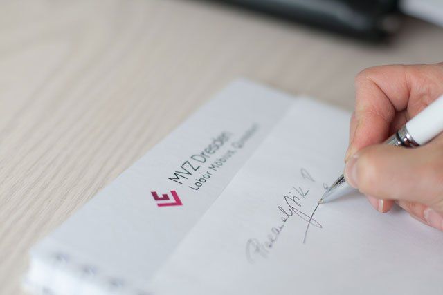 Handsignierung eines Dokuments mit dem Logo „MVZ Dresden Labor Medizin GmbH“ im Hintergrund.