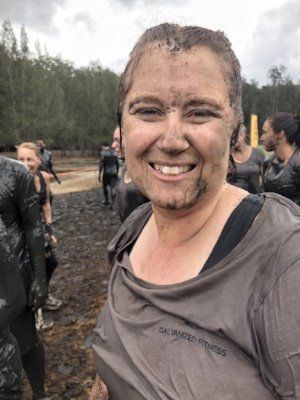 A woman with a lot of mud on her face is smiling.