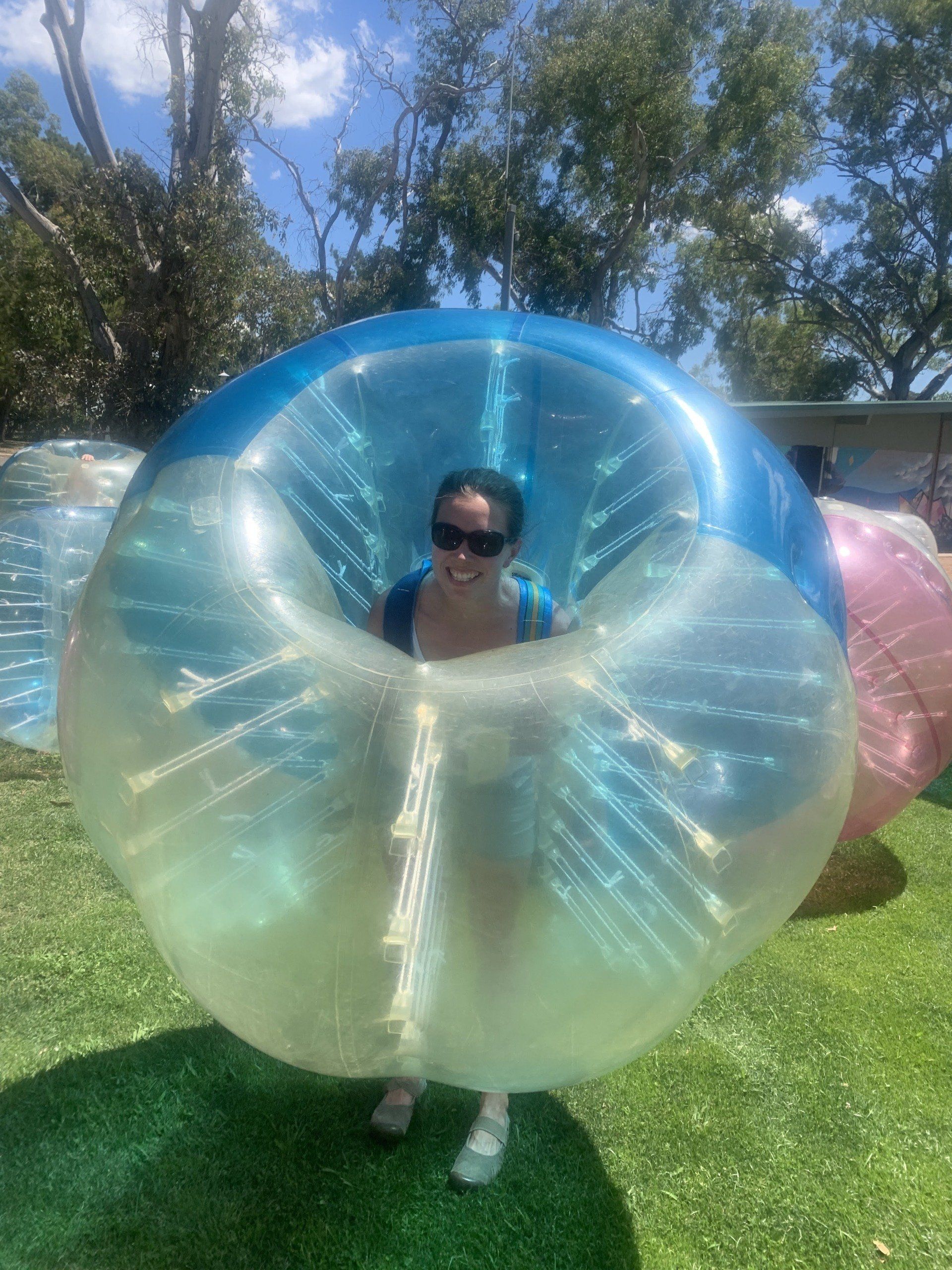 A woman is standing inside of an inflatable bubble ball.