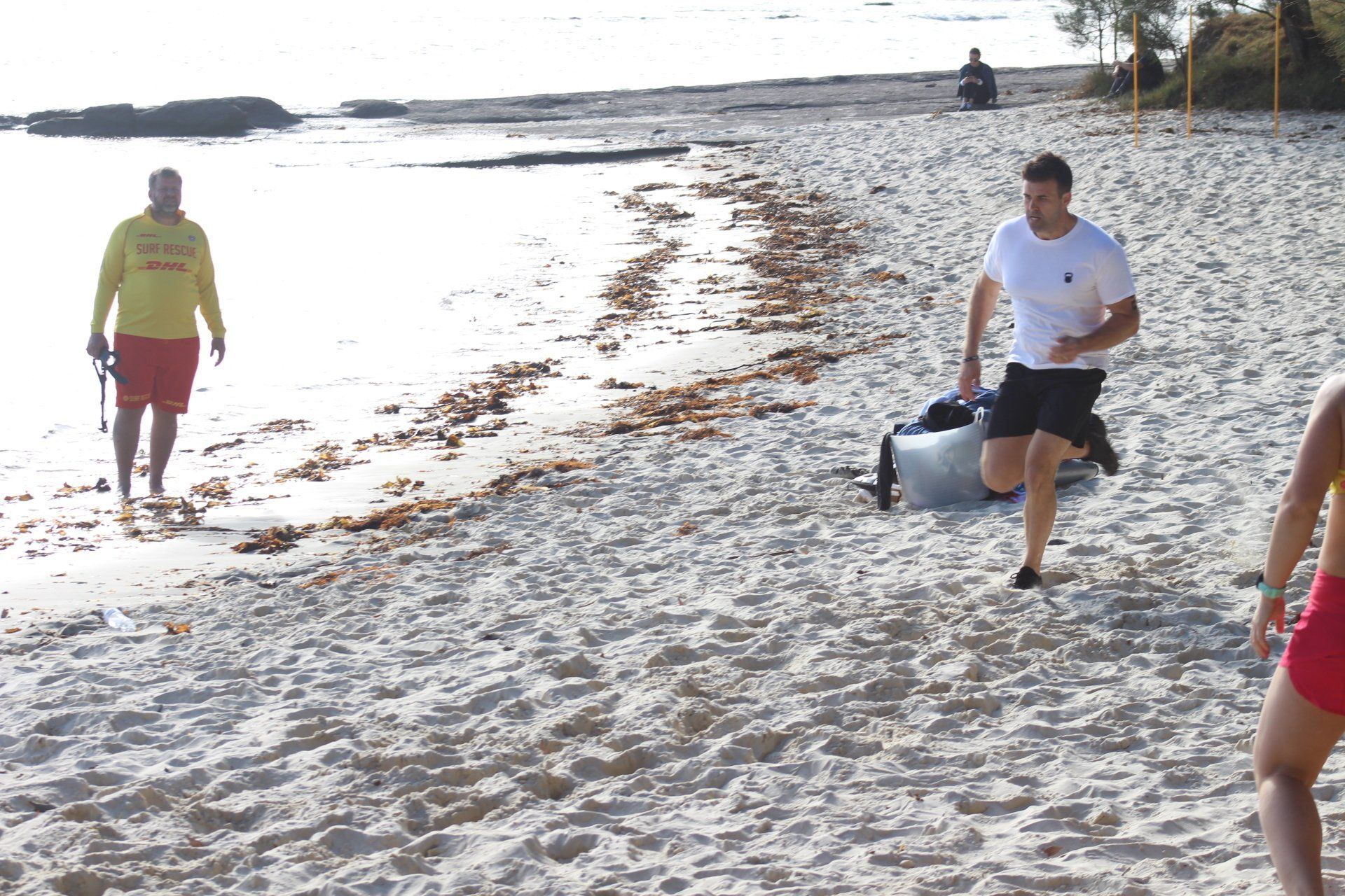 A man carrying a bag on a beach with a lifeguard in the background