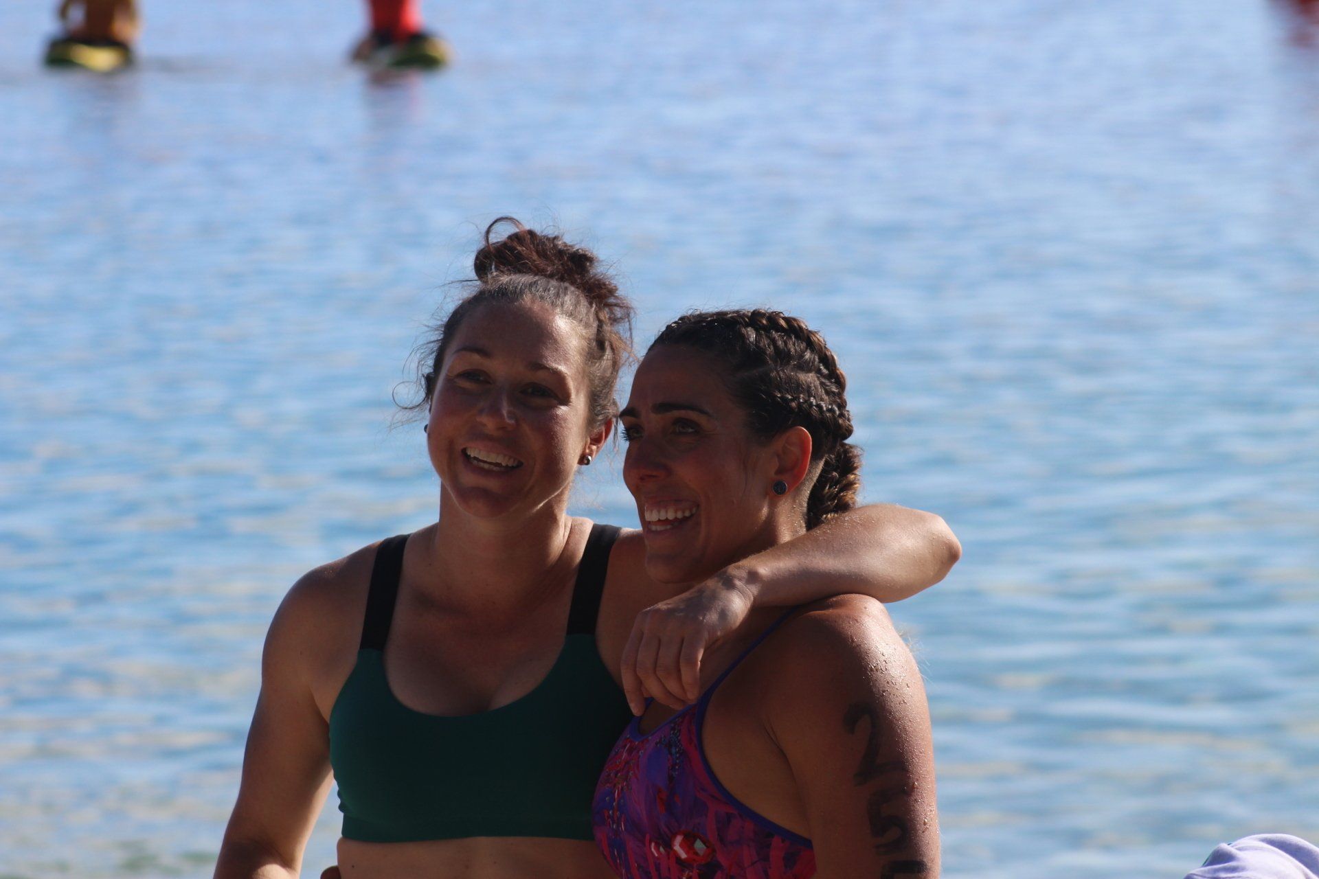 Two women are posing for a picture on the beach.