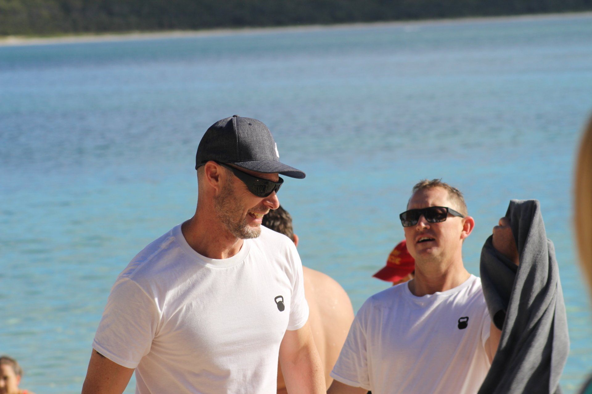 Two men are standing on a beach next to a body of water.