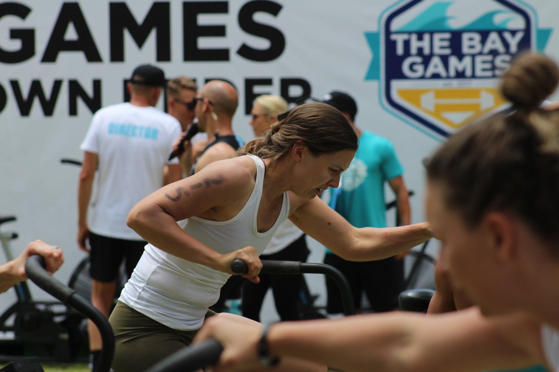 A group of people are riding exercise bikes in front of a sign that says the bay games