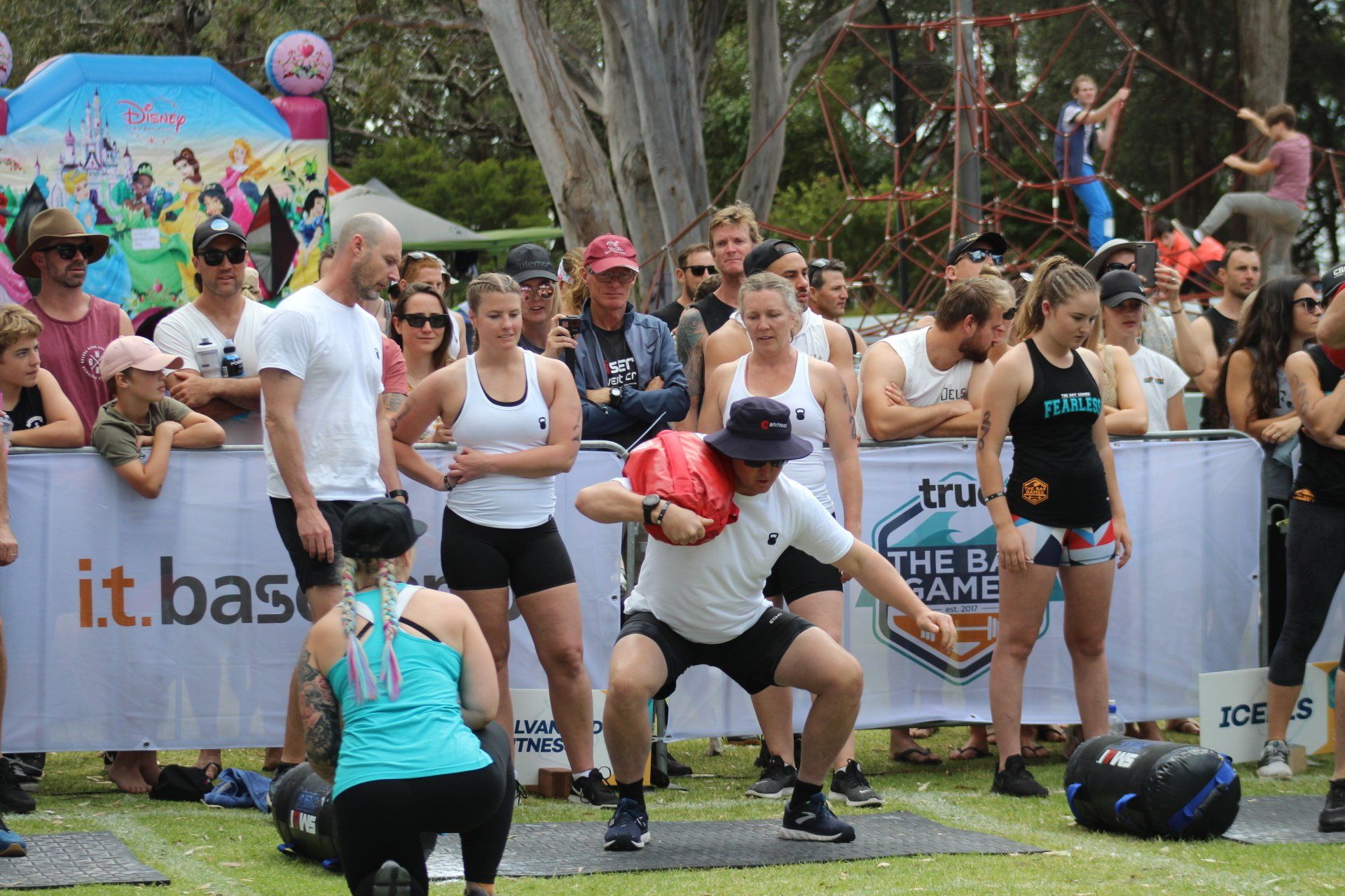 A group of people are watching a man squatting with a bag on his head.