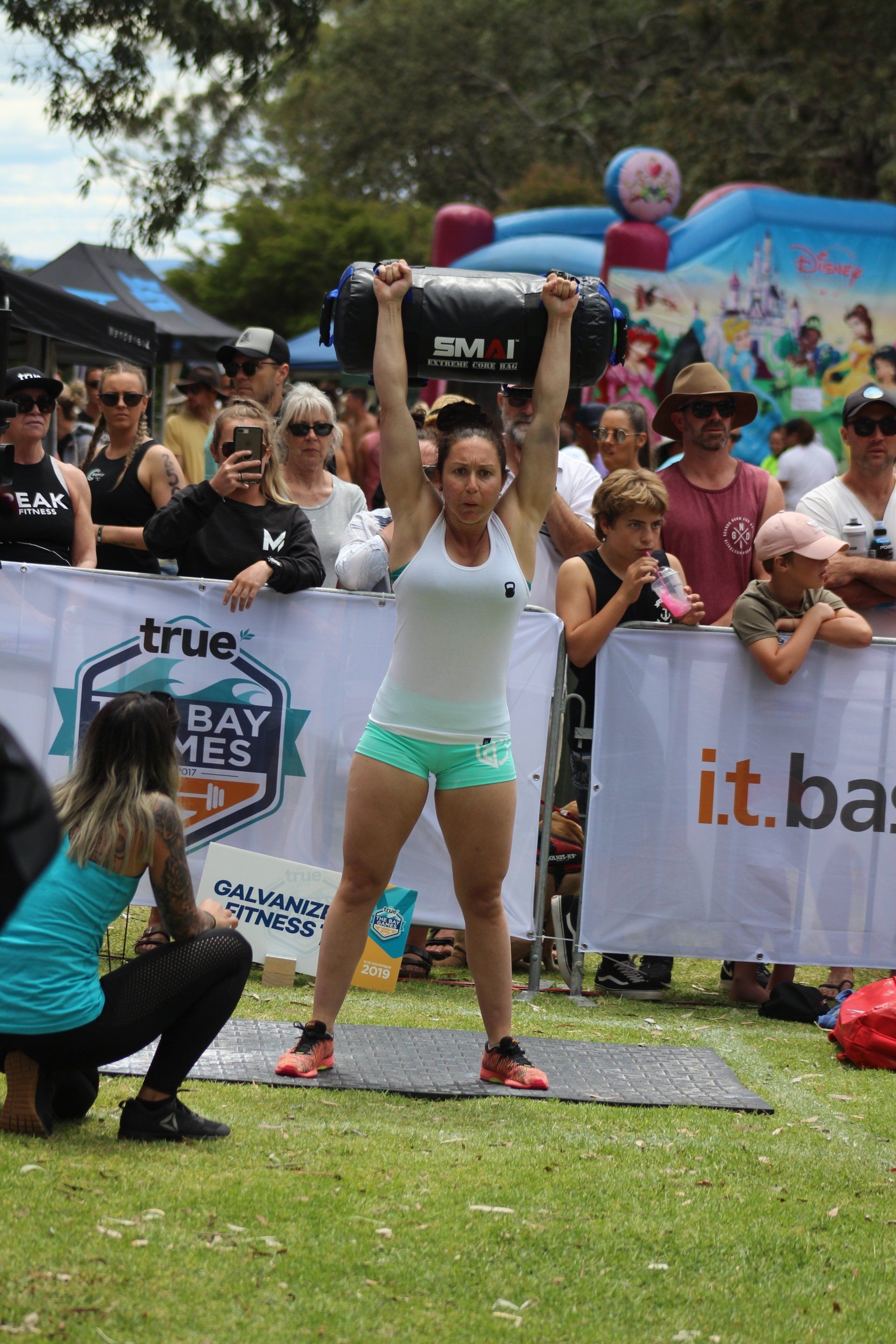 A woman is lifting a large bag over her head in front of a crowd.