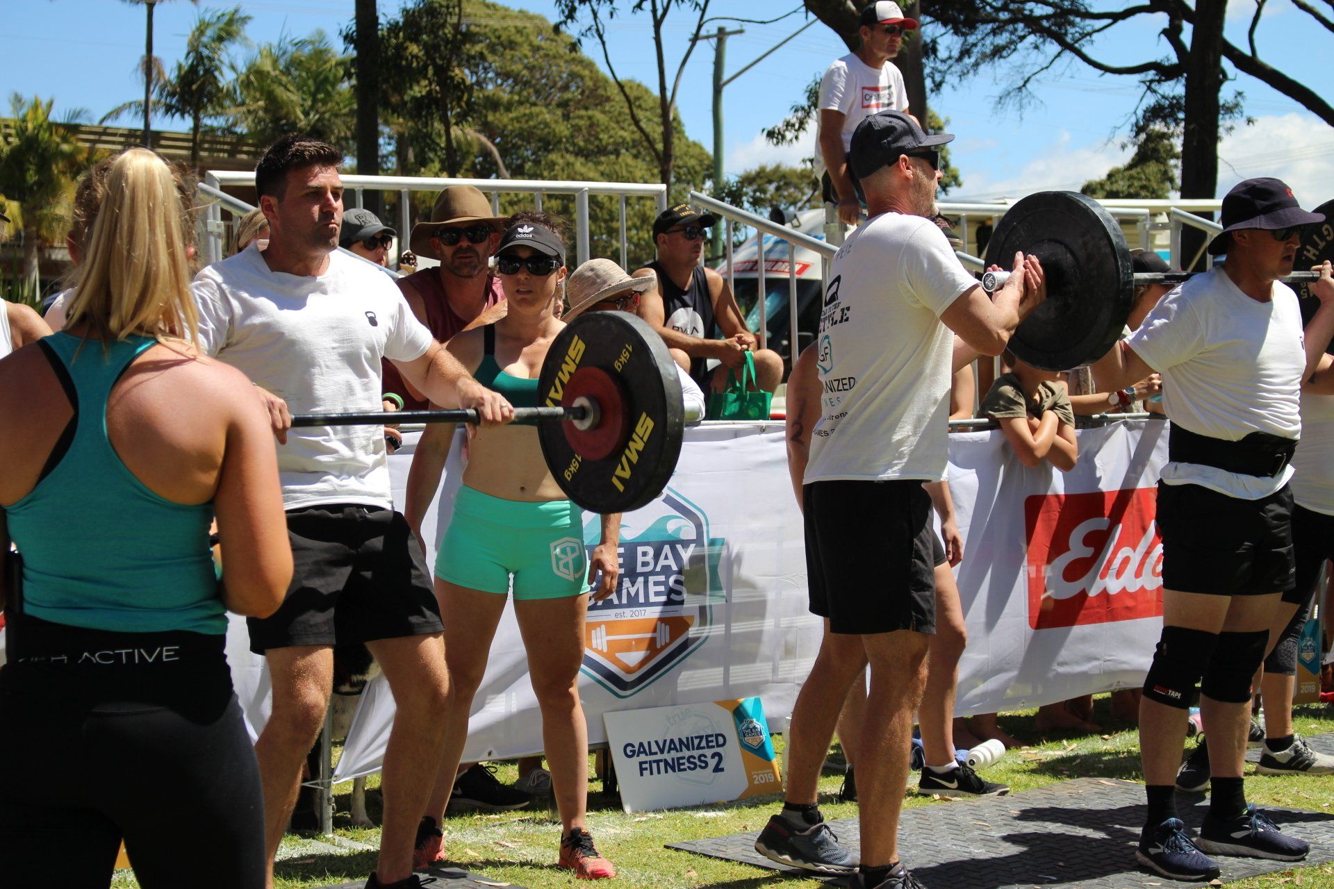 A group of people are standing around a barbell in a park.