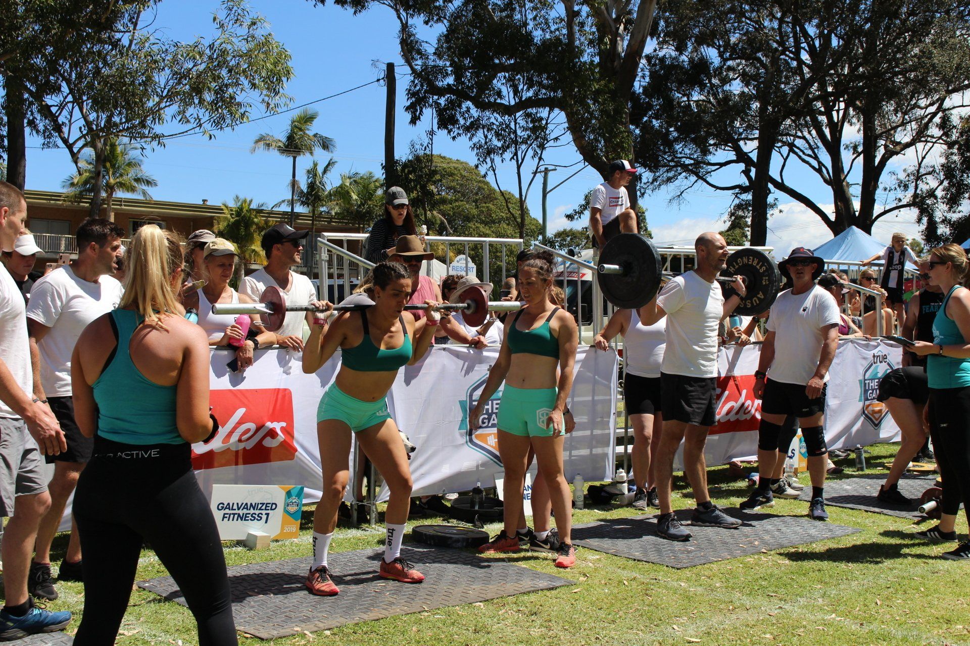 A group of people are standing around a woman lifting a barbell.