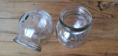 Twee lege, doorzichtige glazen cuppingbekers staan ​​op een lichtbruine houten ondergrond.