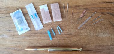 Een verzameling gouden, metalen en blauwe medische of acupunctuurinstrumenten en -benodigdheden, uitgestald op een houten ondergrond.