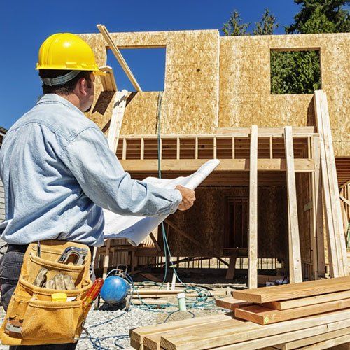 Man in hard hat inspecting a building under construction while looking at a plan